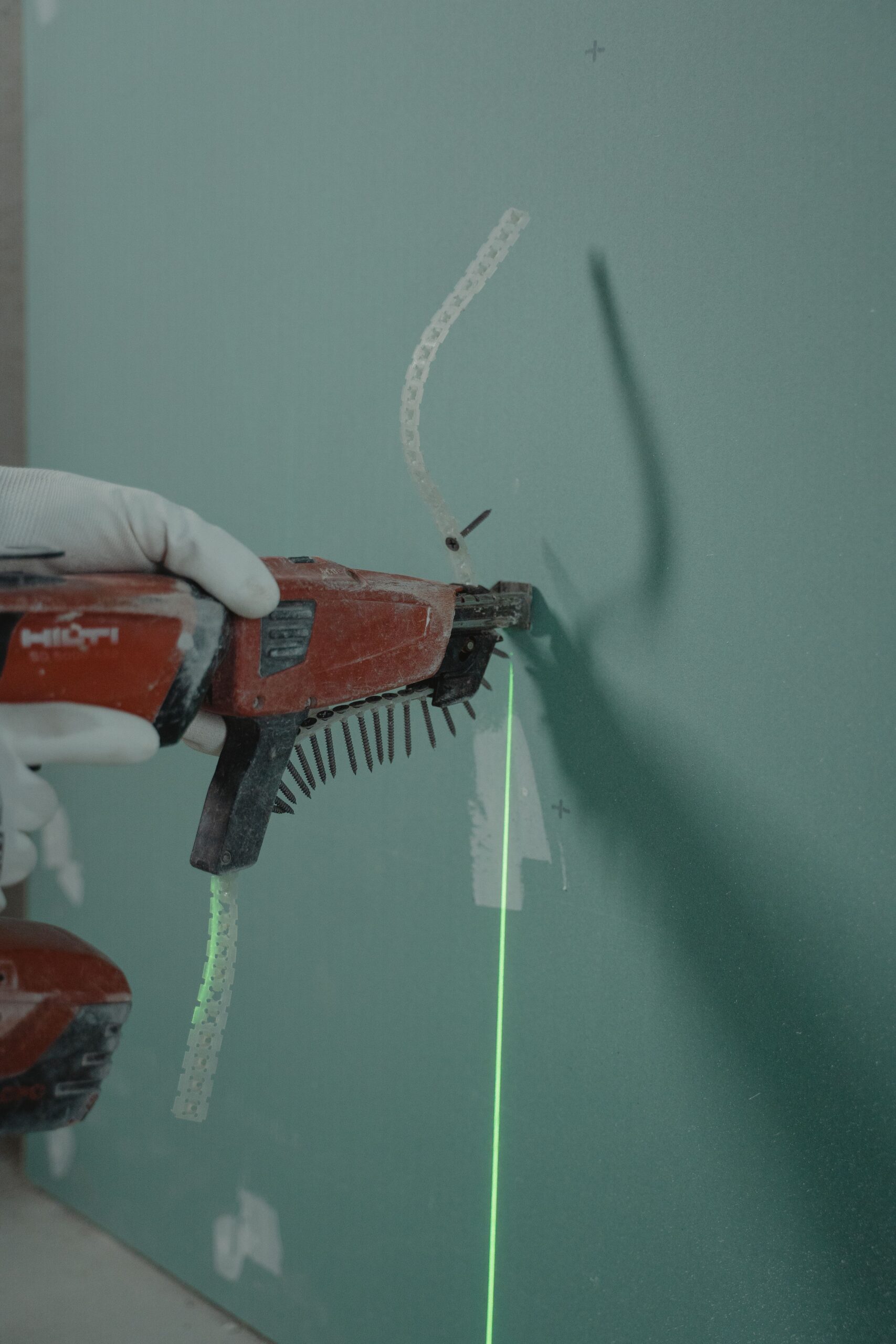 Home Close-up of a handyman using a laser level and nail gun for drywall installation.
